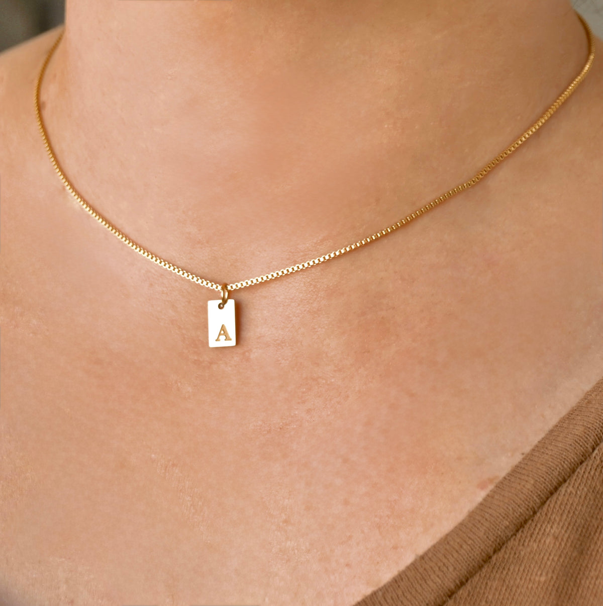 Gold box chain necklace with a rectangle pendant featuring the letter 'A' on a person's neck.