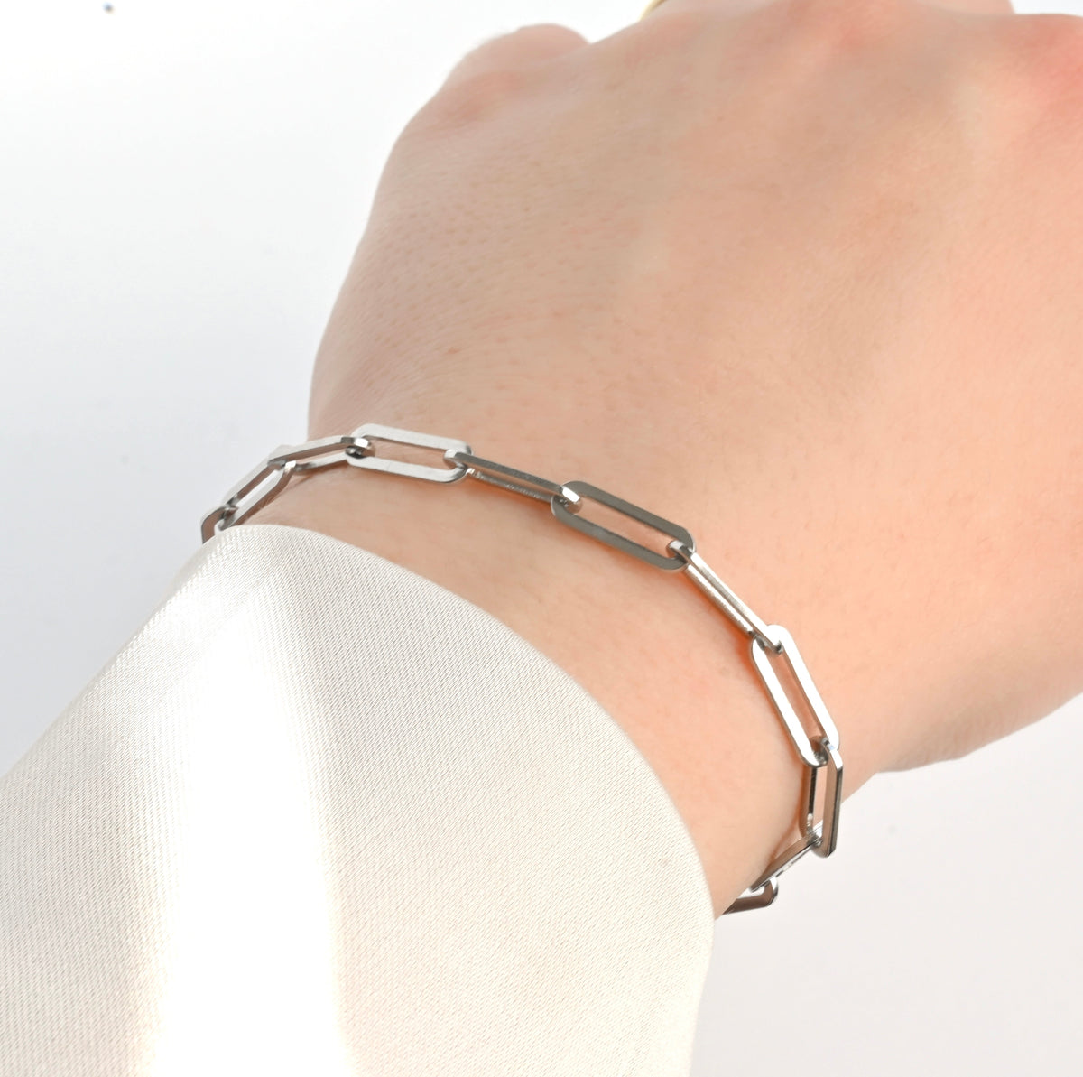 Silver paperclip bracelet on a wrist with a plain background