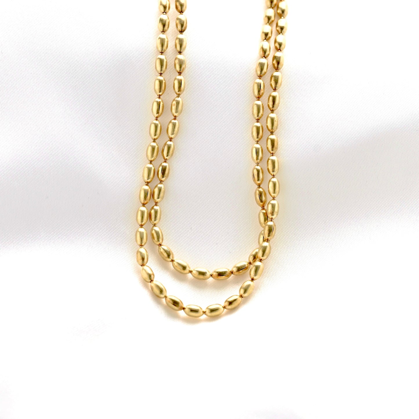 A gold chain necklace with elongated, polished oval links, draped in two loops against a white background.