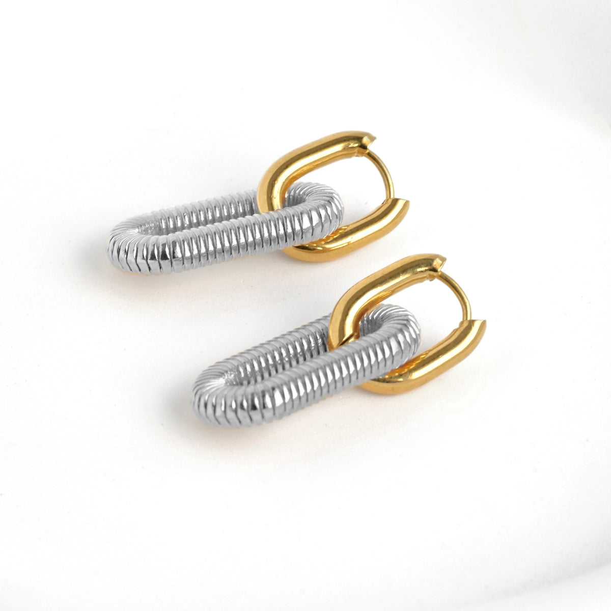 Pair of two tone earrings with gold U shaped hoop with clicker closure and an attached silver textured link on a white background