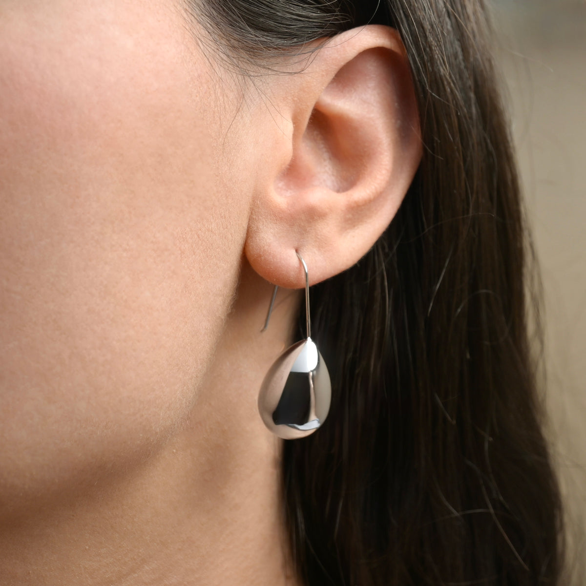 Close-up of an ear wearing a large teardrop-shaped earring with a blurred background