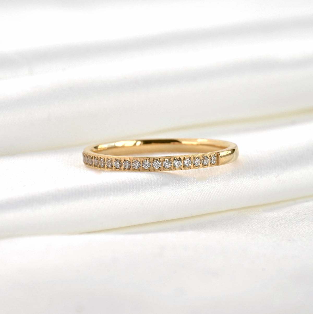 Close-up view of thin pave ring on white satin background.