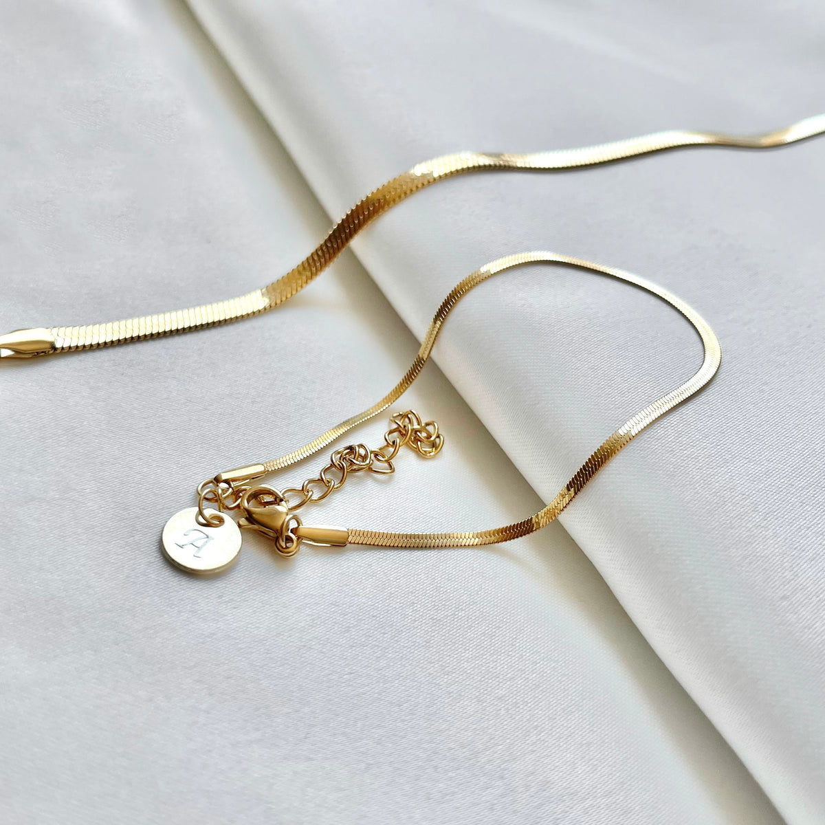 Gold bracelet with a small round initial charm on a light gray background