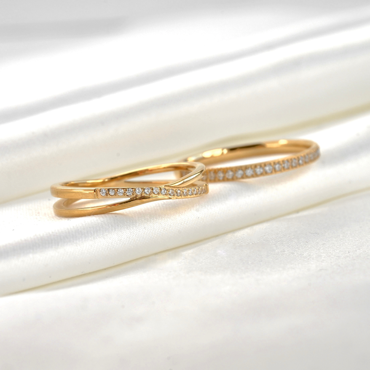 Gold rings, one X shaped the other half eternity band, with pave diamonds on a white satin background