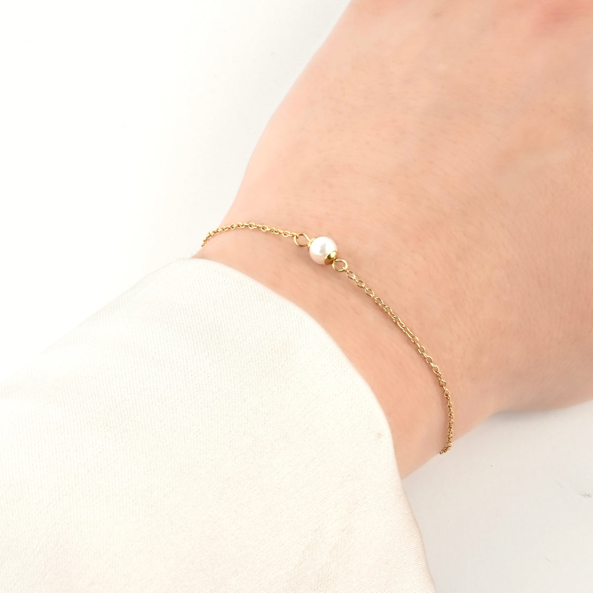 Gold single pearl bracelet on a wrist against a white background
