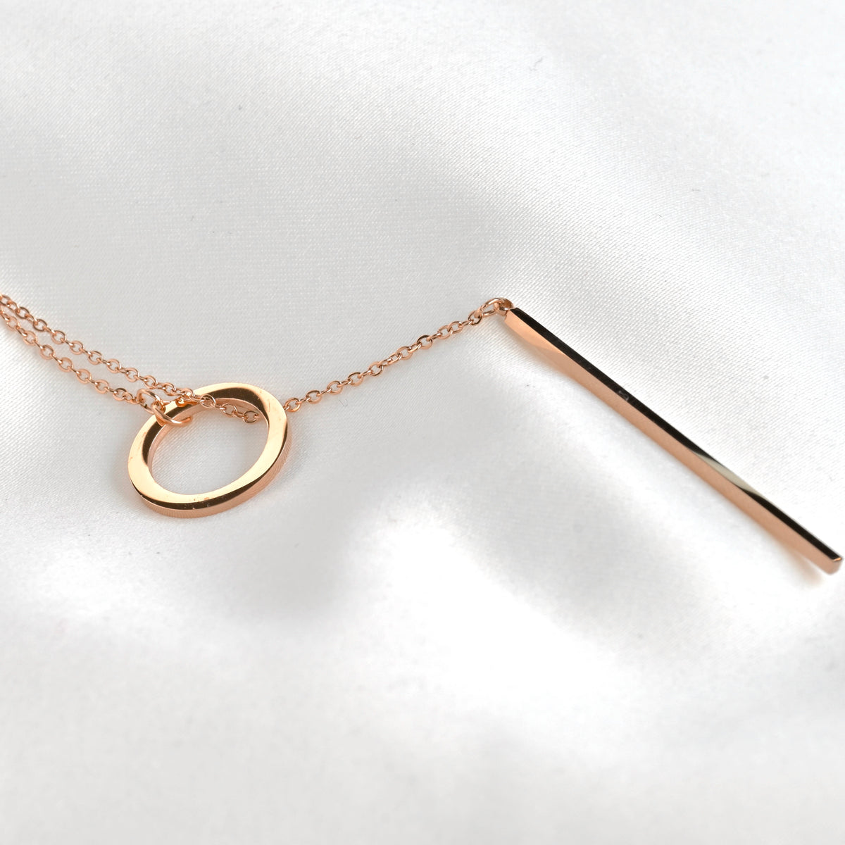 Rose gold necklace with a circular pendant and a straight bar threaded in the circle on a white background