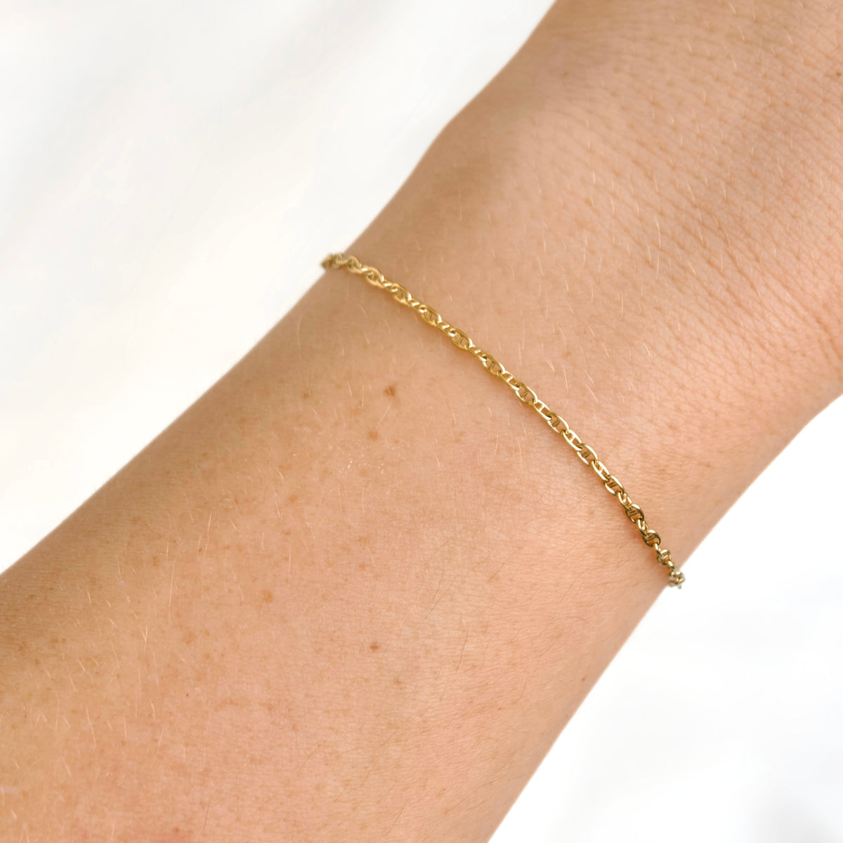 A delicate yellow gold mariner chain bracelet worn on a person's wrist, shown in a close-up shot against a bright white background.