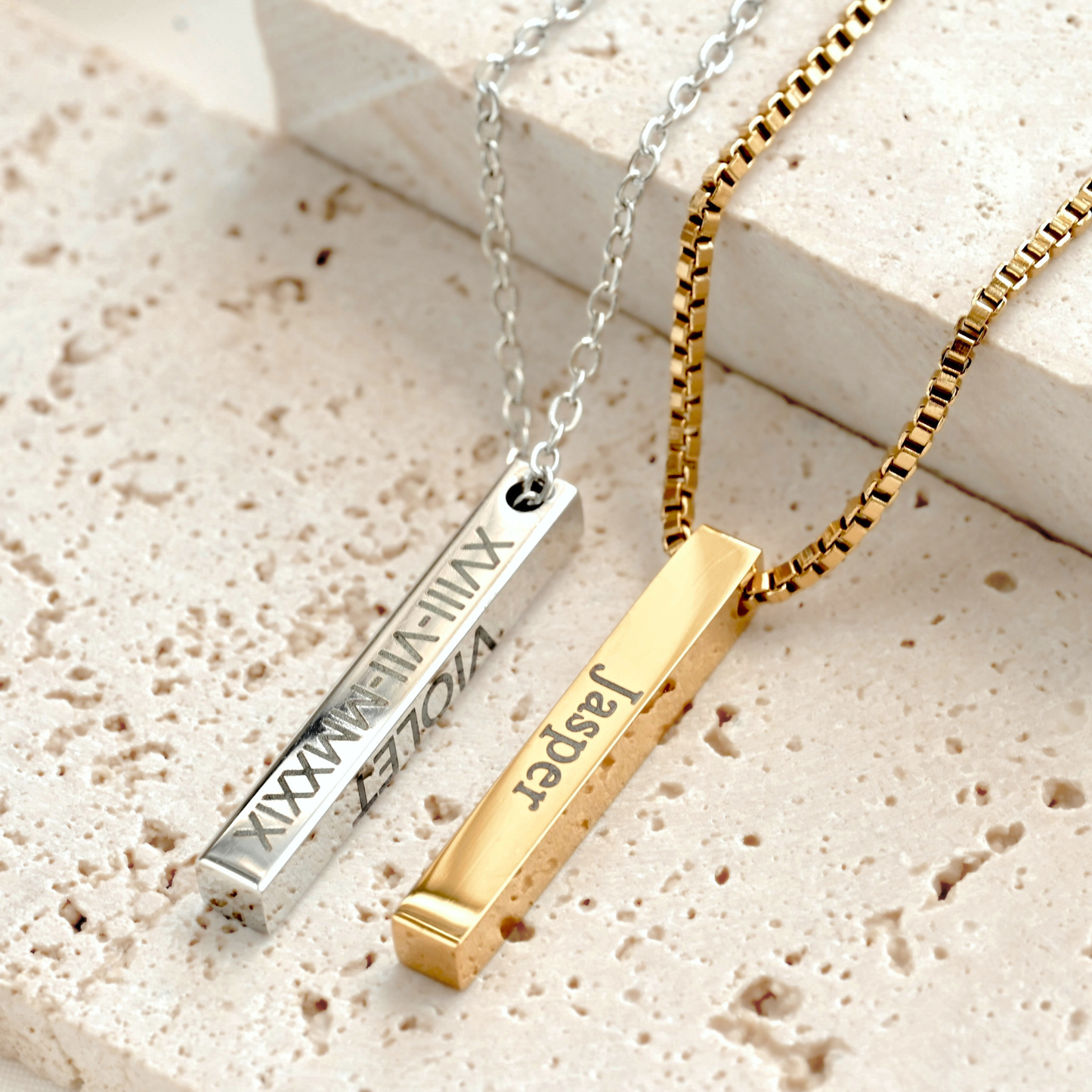 Gold and silver personalized bar necklaces with engraved names and roman numerals on a textured surface
