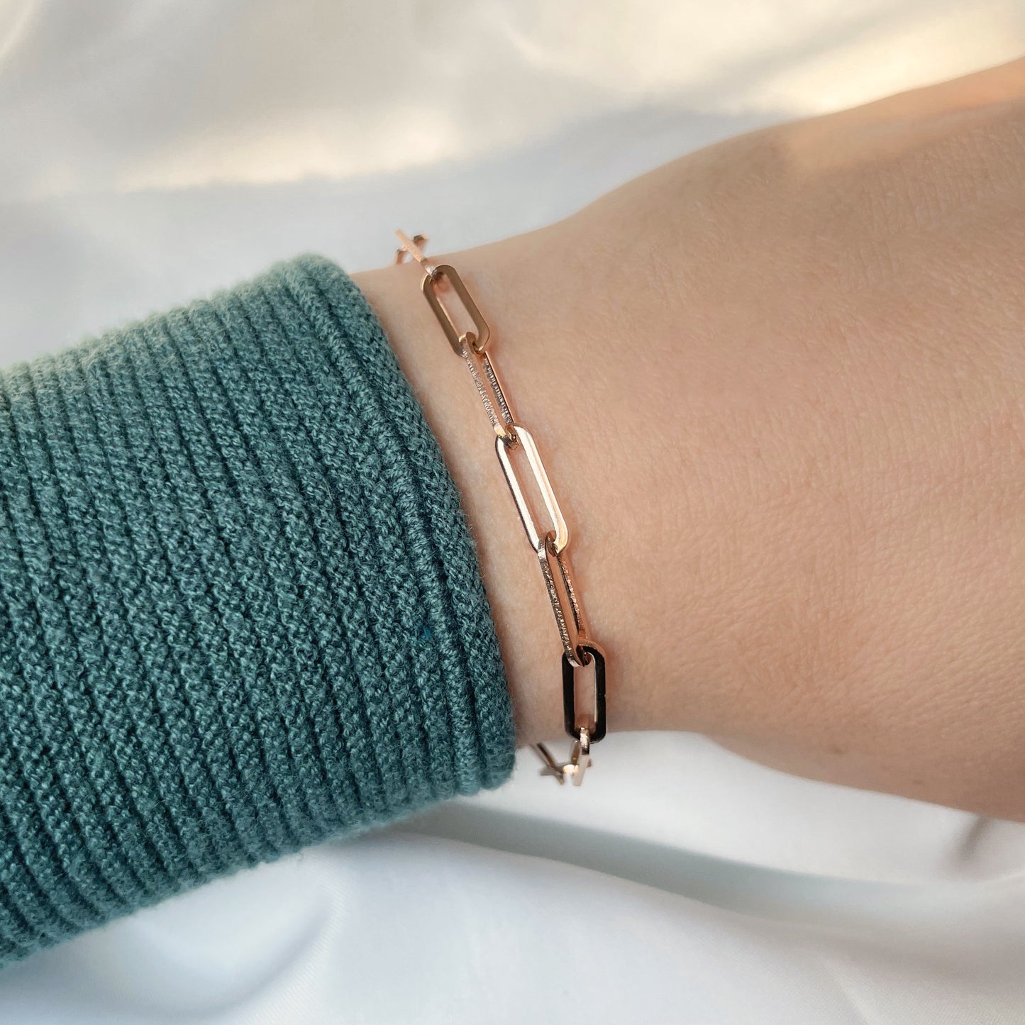 Bold Rose gold paperclip chain bracelet on a wrist with a green sleeve against a white background