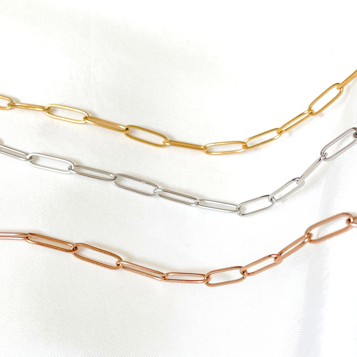 Three gold, silver, and rose gold link chain necklaces on a white background