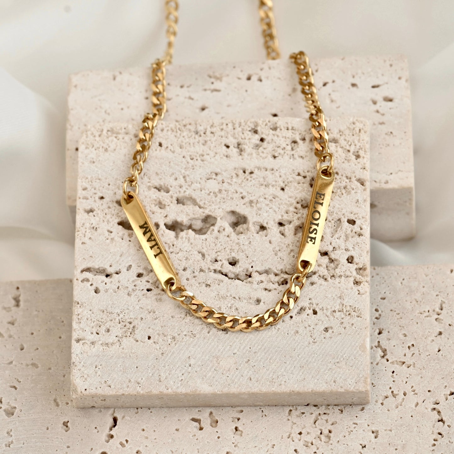 Gold curb chain bracelet with names on a textured stone surface