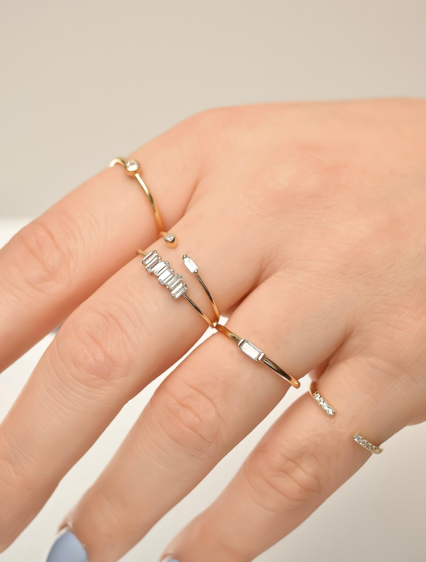 Close-up of a hand wearing stacked gold rings on a neutral background