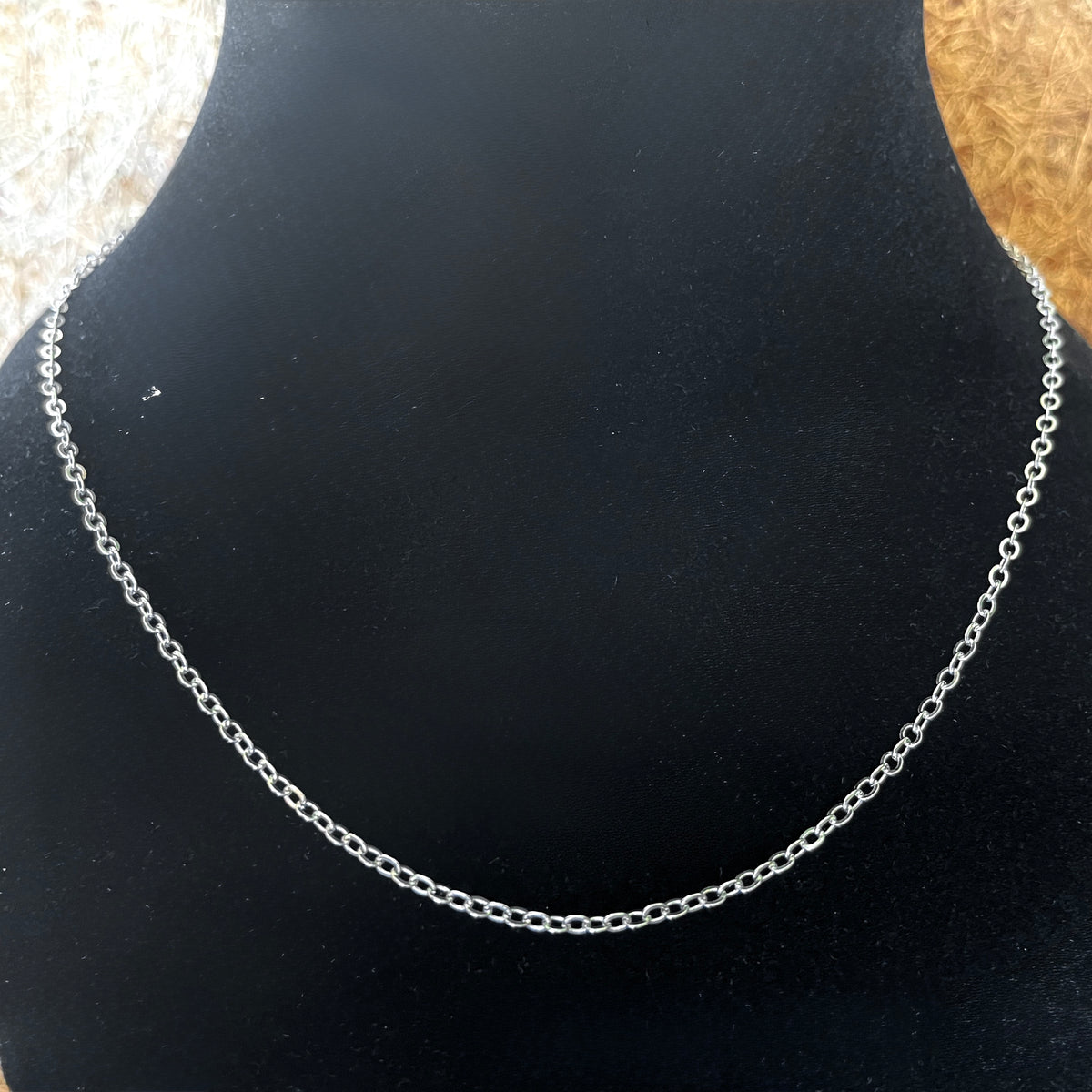 Silver cable chain necklace on a black stand