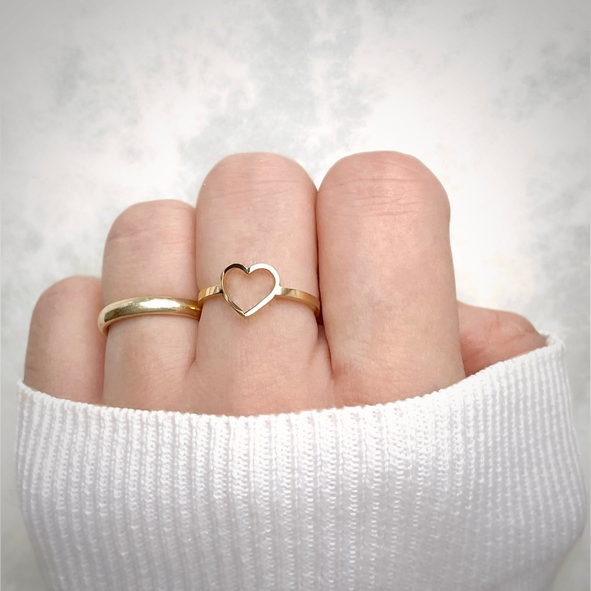 Gold heart-shaped ring with a flat slim band on a finger against a white background