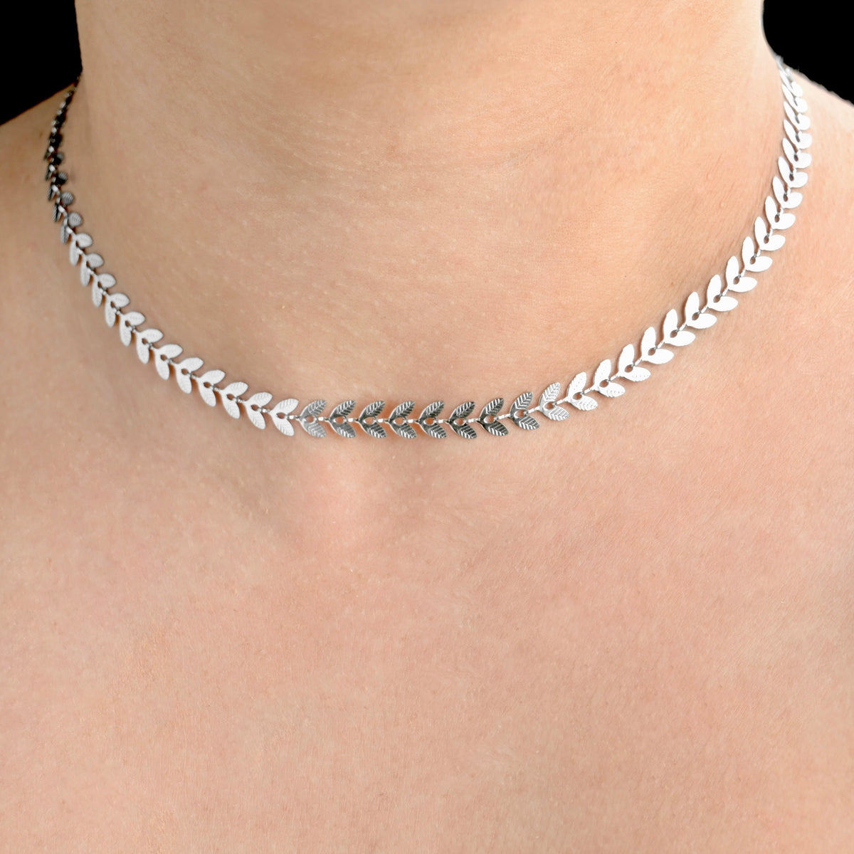 Silver leaf necklace on a person's neck against a neutral background