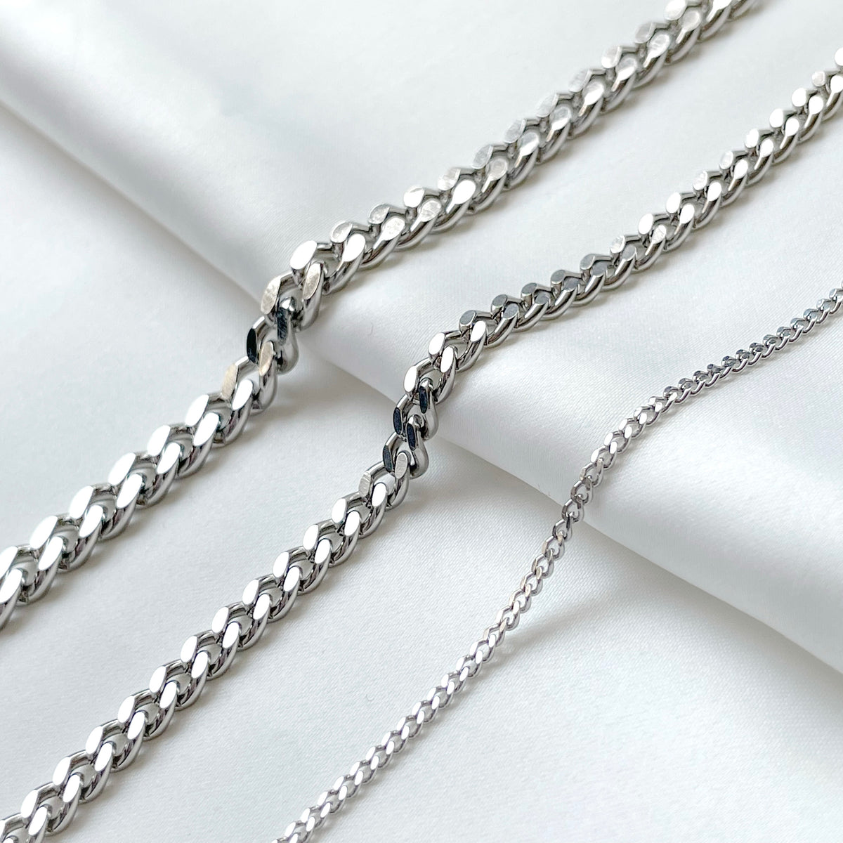 Three silver curb chains of different thicknesses on a light background