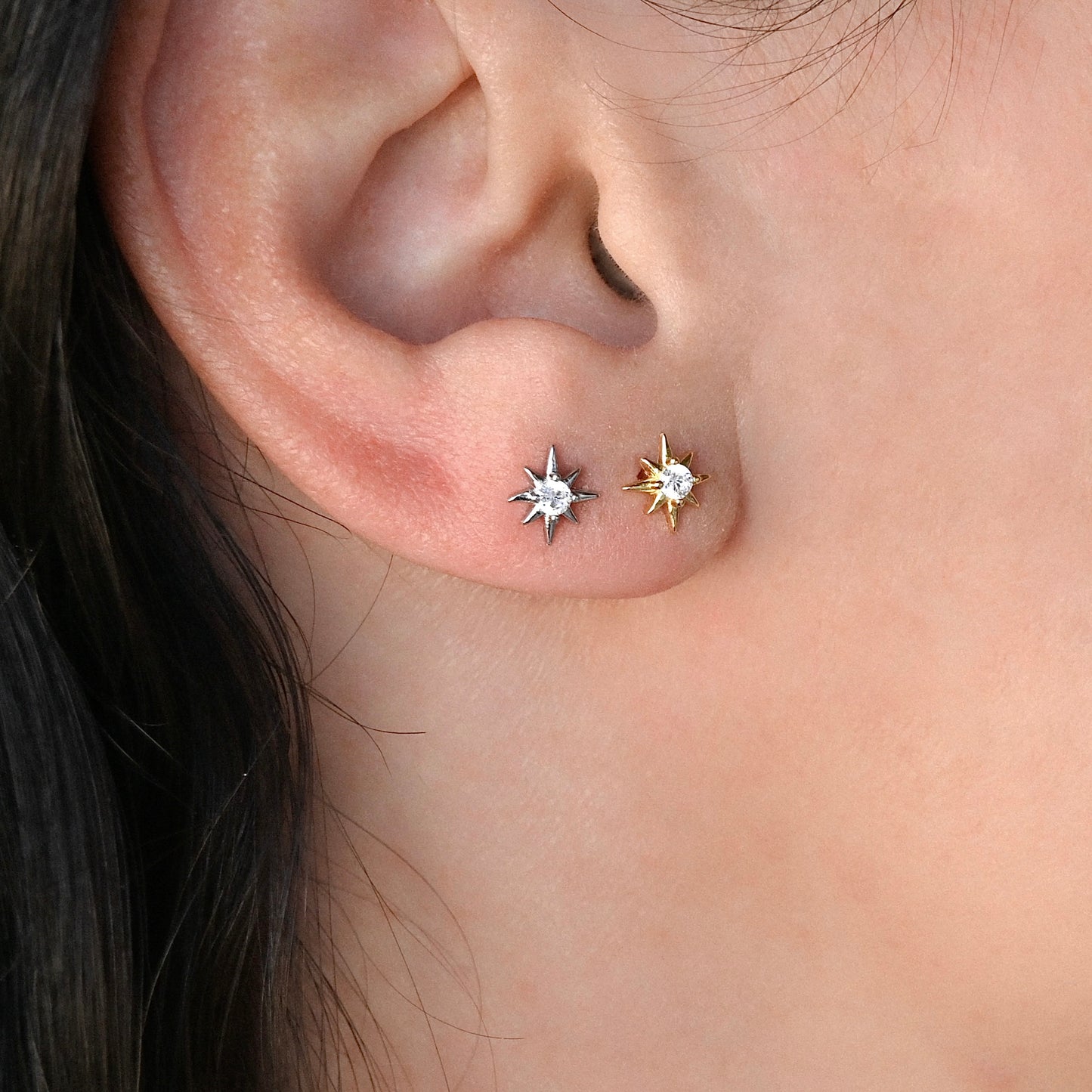 Close-up of an ear wearing two star-shaped CZ studs, one gold and one silver