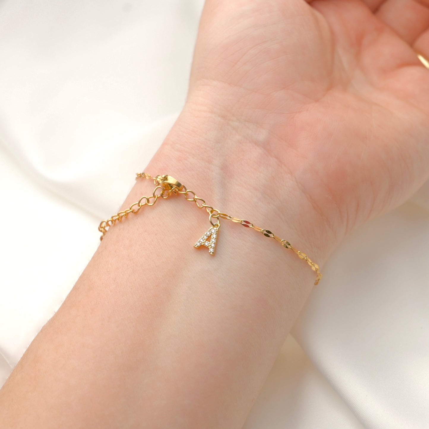 Dainty Gold chain bracelet with a letter 'A' charm adorned with diamonds on a wrist against a white background