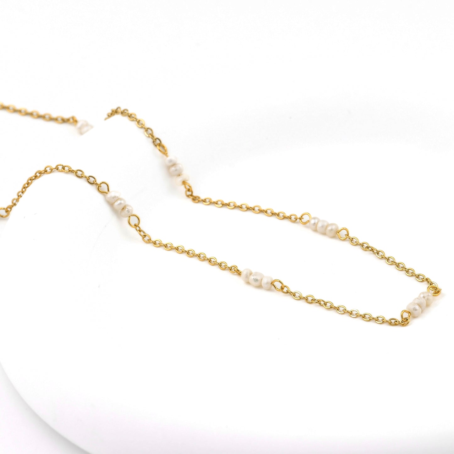 Gold chain necklace with tiny pearls on a white background