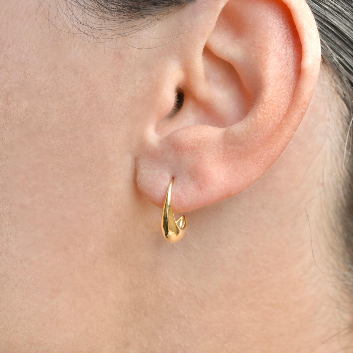 Small gold hoop earring worn by a person