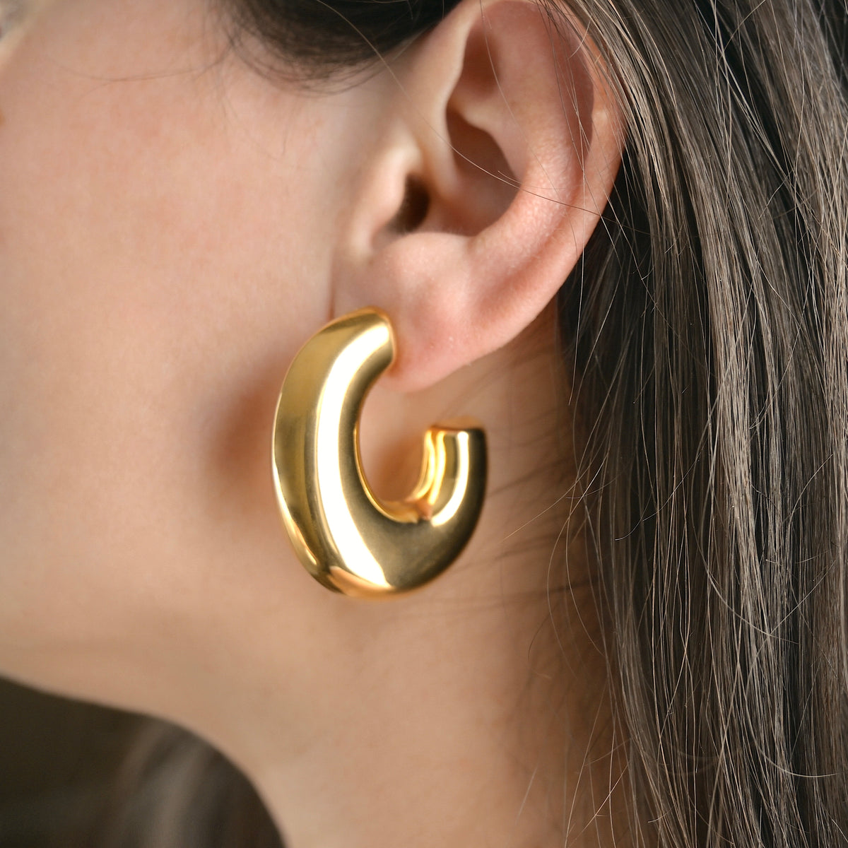 Oversized statement Gold hoop earring worn by a person with brown hair.