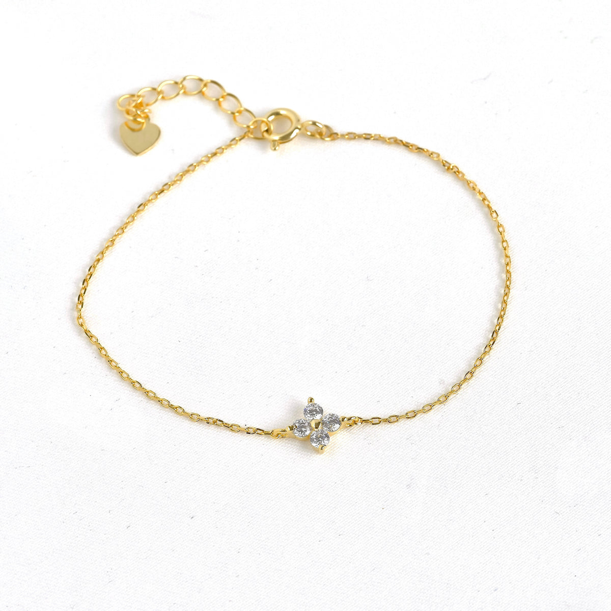 Top view of gold 4 leaf clover CZ bracelet with a small heart charm on a white background