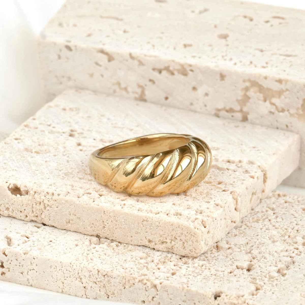Thick gold twisted dome ring on a stone surface with a white background