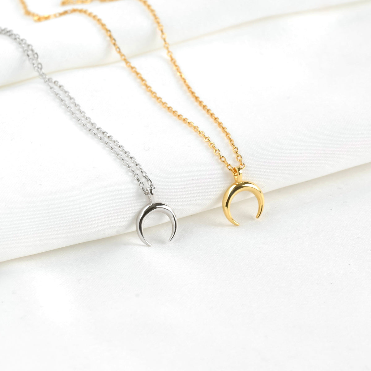 Two necklaces with crescent moon pendants on a white surface