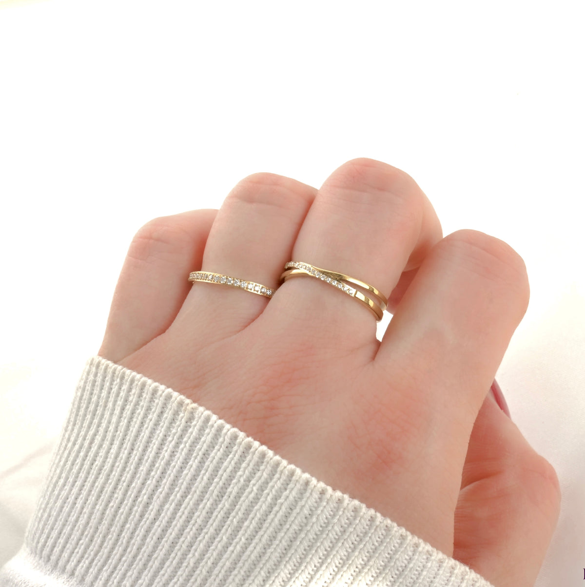 Hand wearing a crossover ring and a half eternity band side by side on a white background