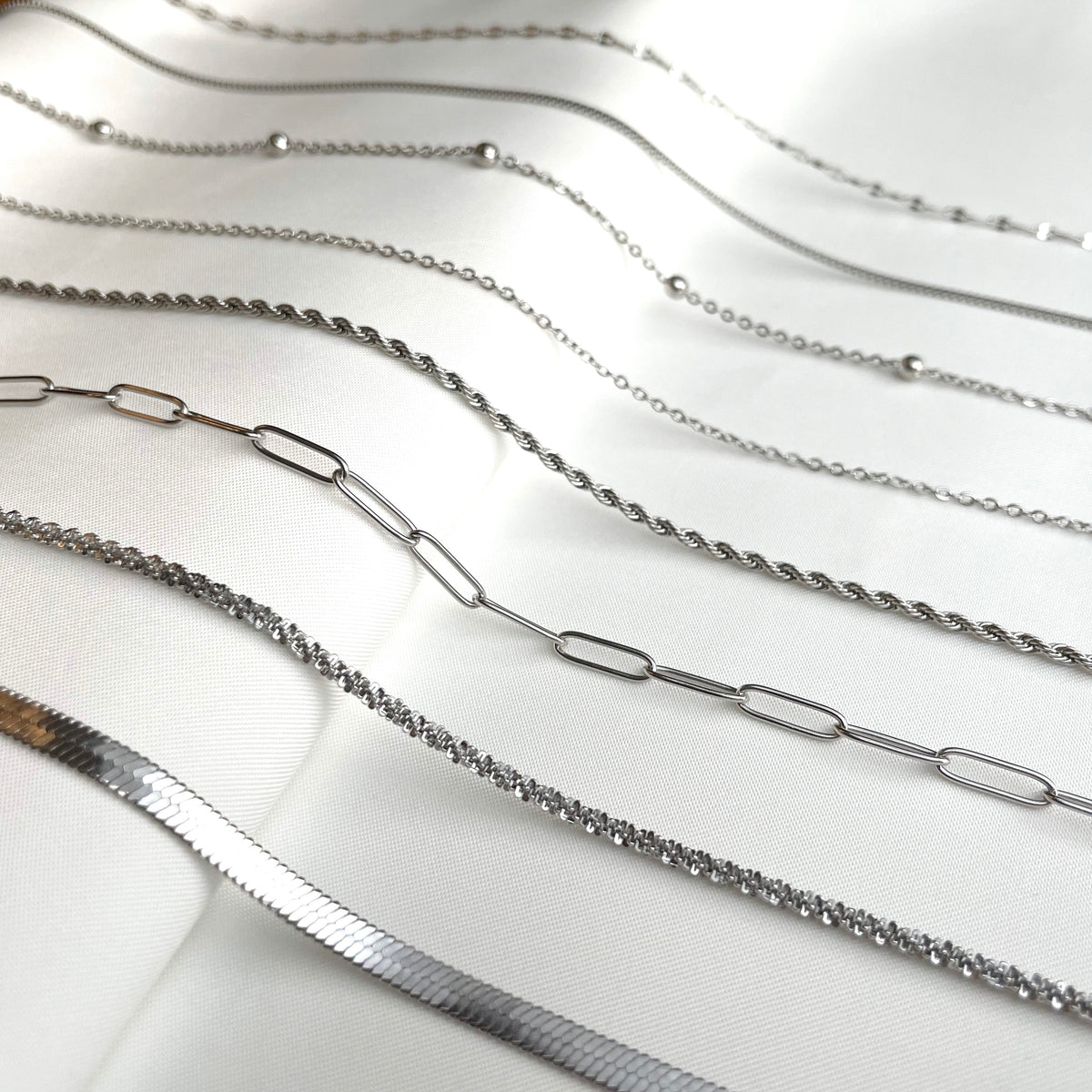 Collection of various dainty silver chain necklaces on a white background
