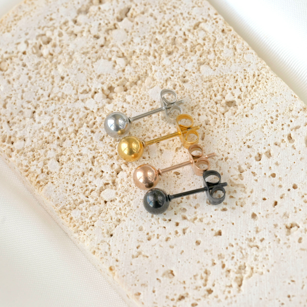 Top view of set of small round stud earrings in various colors on a textured beige surface