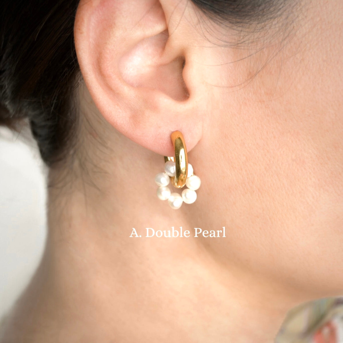 Gold hoop earring with white pearl charm circle worn by a person