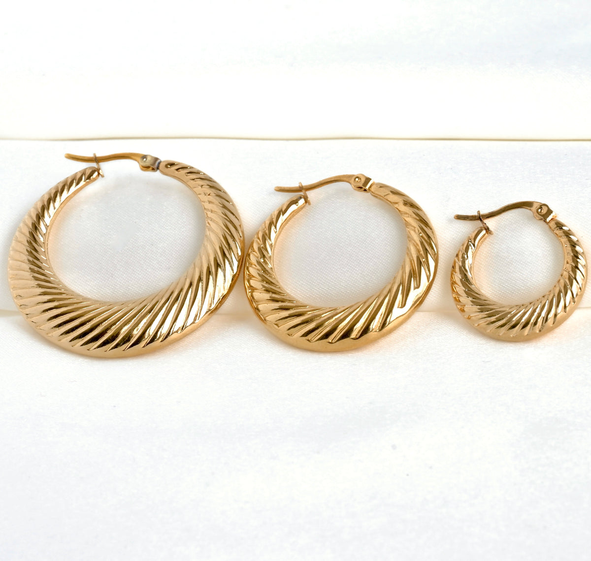 Three gold hoop earrings in three different sizes on a white background