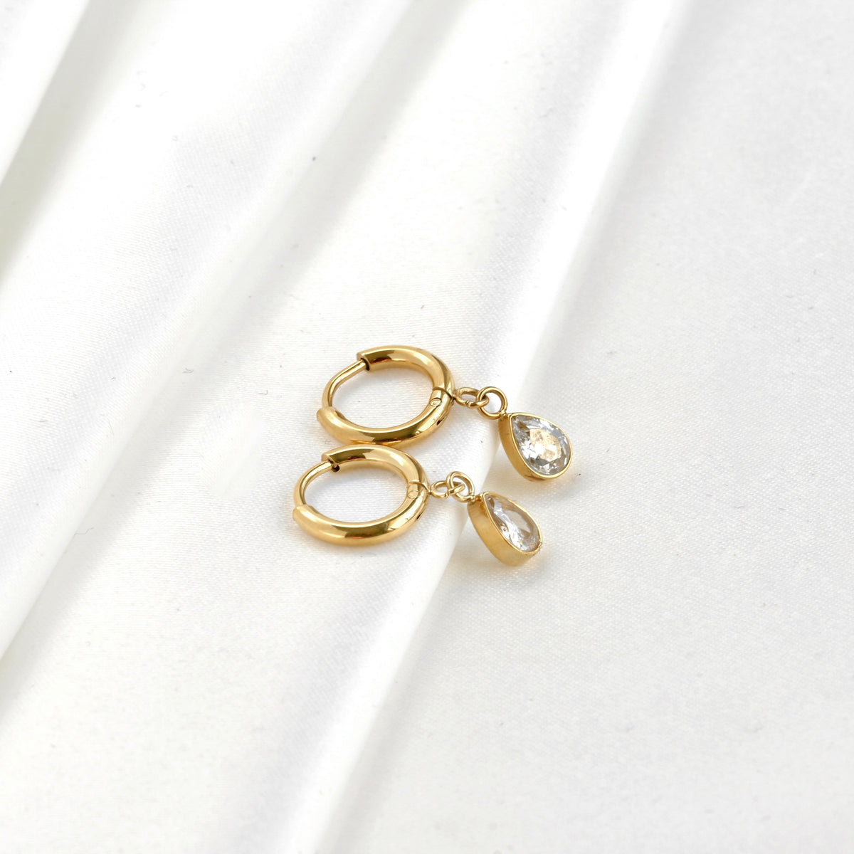 Wide angle view of Gold teardrop diamond charm earrings on a white background