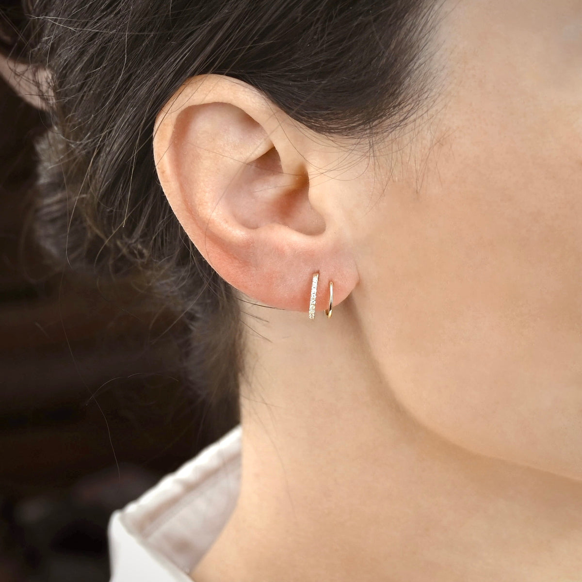 Close-up of an ear wearing pave cz gold spiral hoop earrings with a blurred background