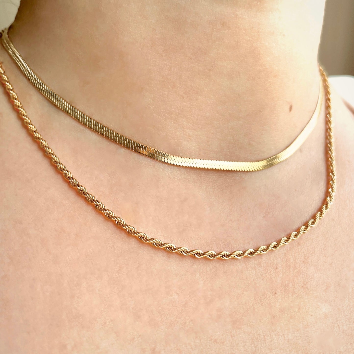 Two gold necklaces layered on a person's neck with a neutral background