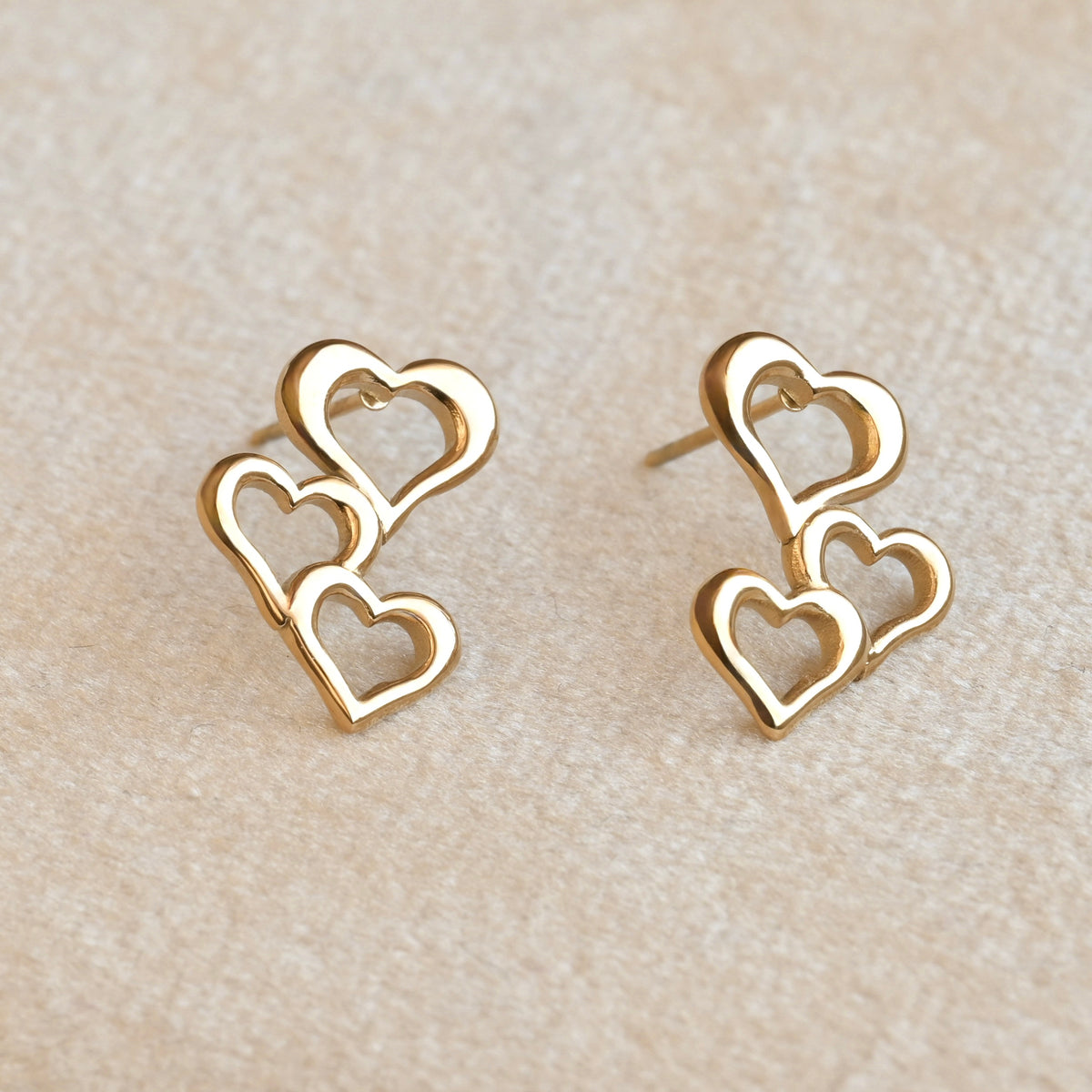 Gold heart drop earrings on a beige fabric background
