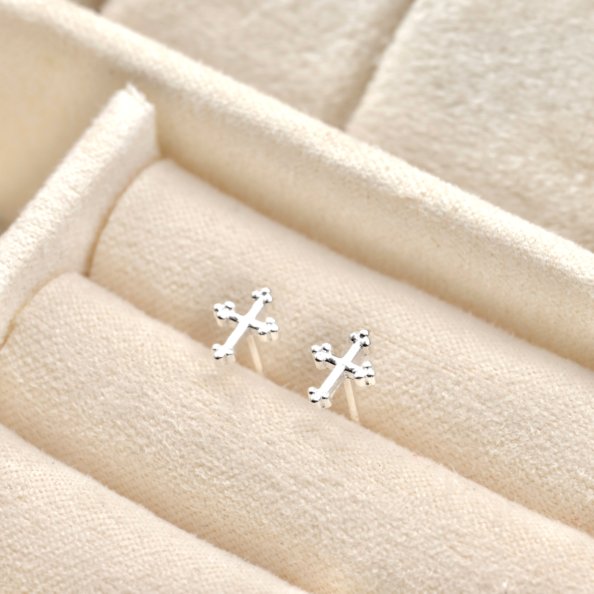 Silver cross studs on a beige fabric background