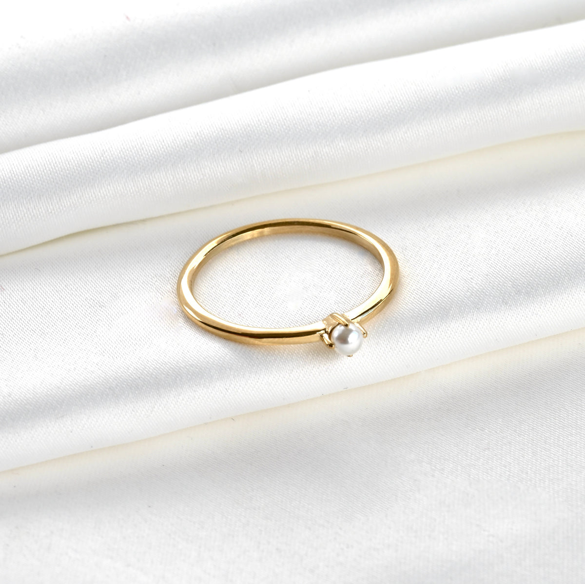 Top view of Gold pearl solitaire ring on a white satin background