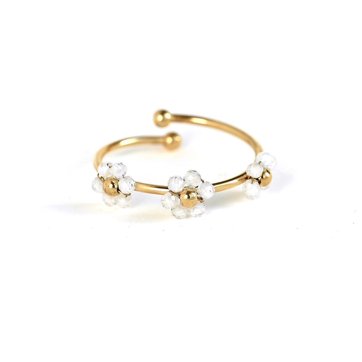 A gold-plated open cuff ring decorated with three small white flower clusters, each featuring a gold center and clear faceted beads, set against a plain white background.