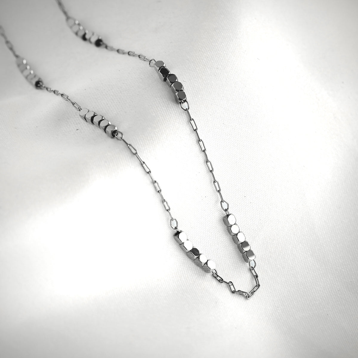 Silver paperclip chain necklace with cube beads on a light gray background