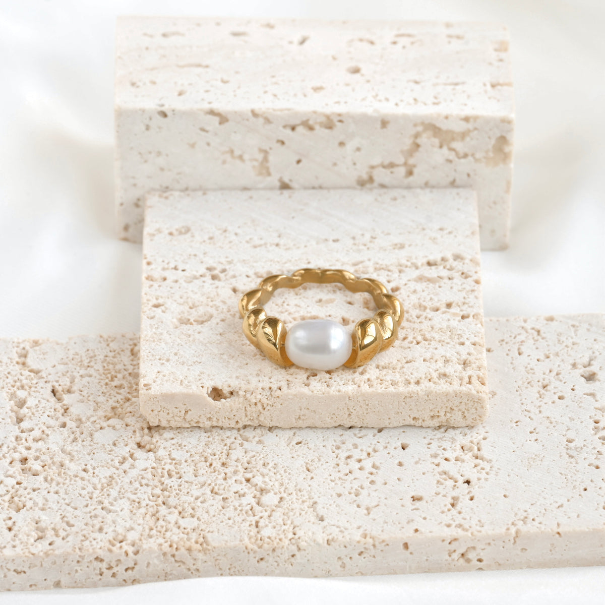 Gold pearl croissant ring on a textured stone surface