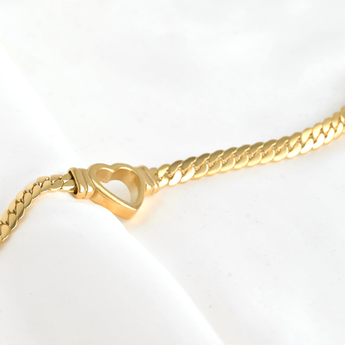 Gold necklace with a thick heart-shaped charm on a white background