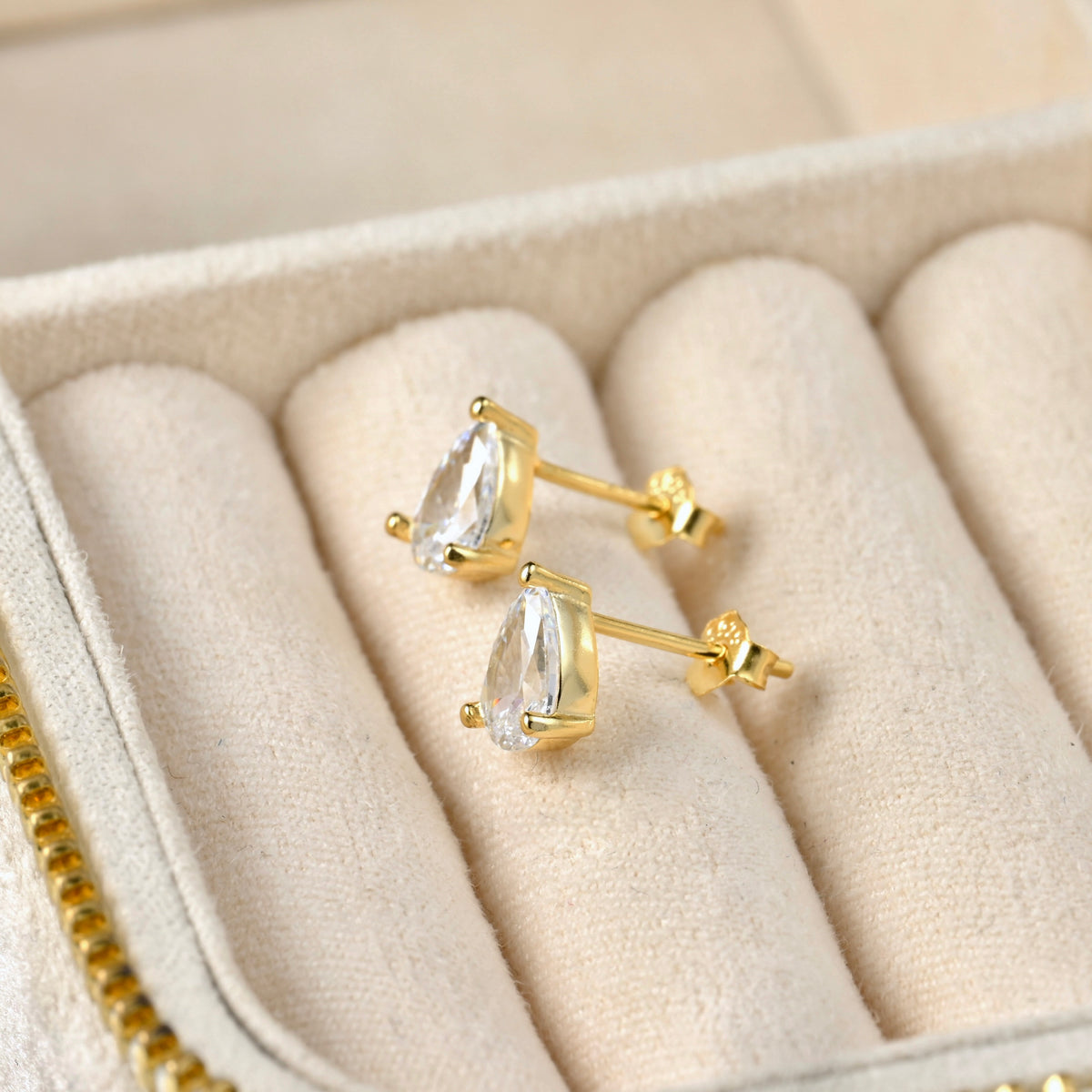 Gold earrings with clear pear-cut gemstones in a jewelry box