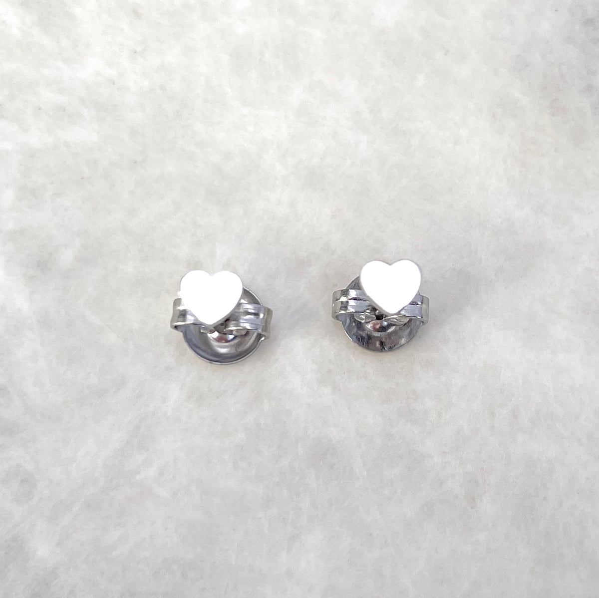 Top view of silver heart earrings standing on butterfly backs on a light gray background