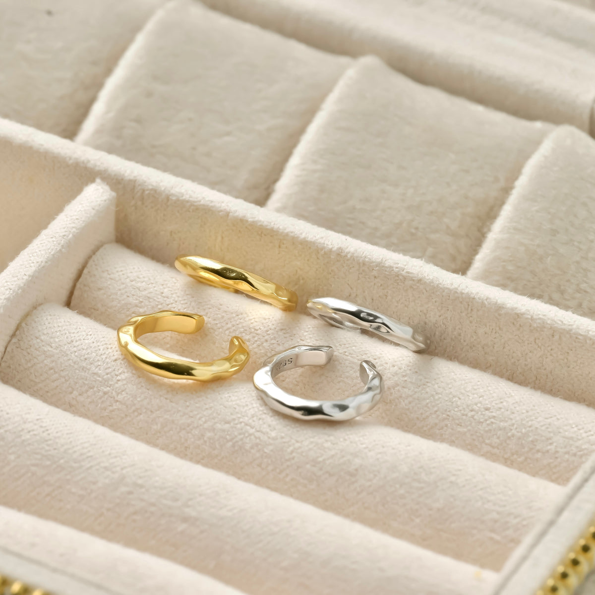 Two pairs of gold and silver textured ear cuffs on a beige jewelry box