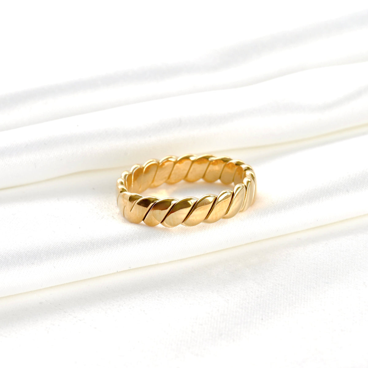 Wide gold ring with a braided design on a white background