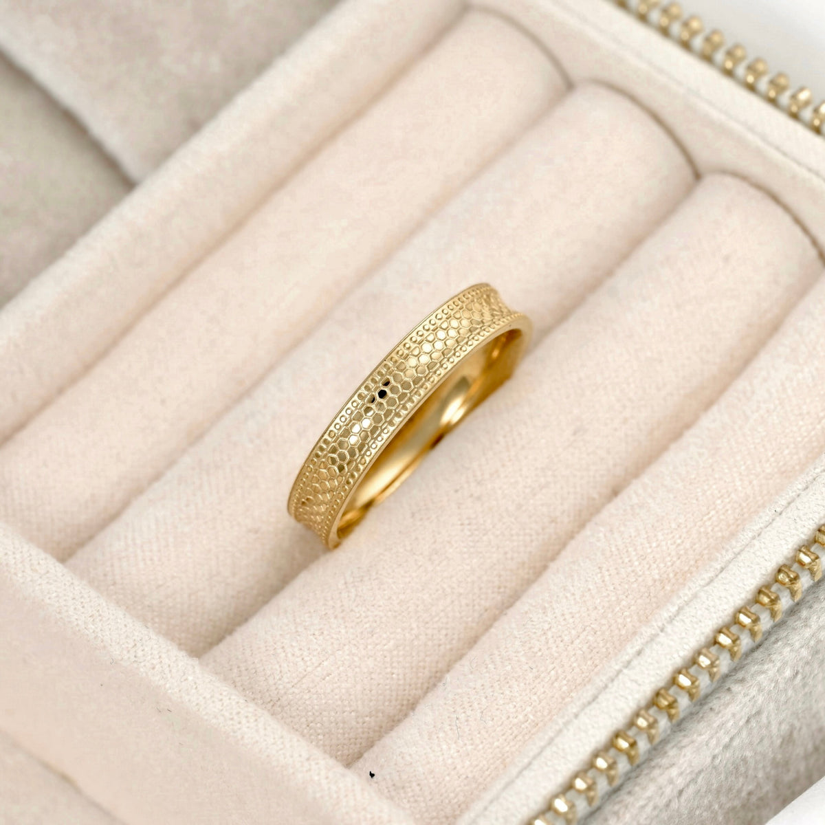 A gold ring with an intricate textured snake skin pattern, displayed inside a cream-colored velvet jewelry box.