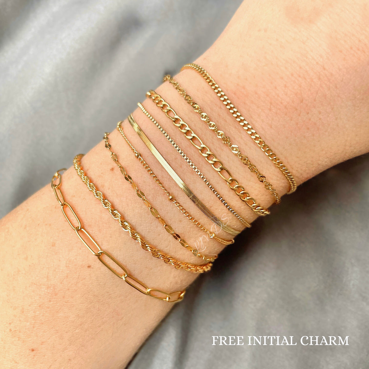 Dainty gold bracelets on a wrist with a neutral background