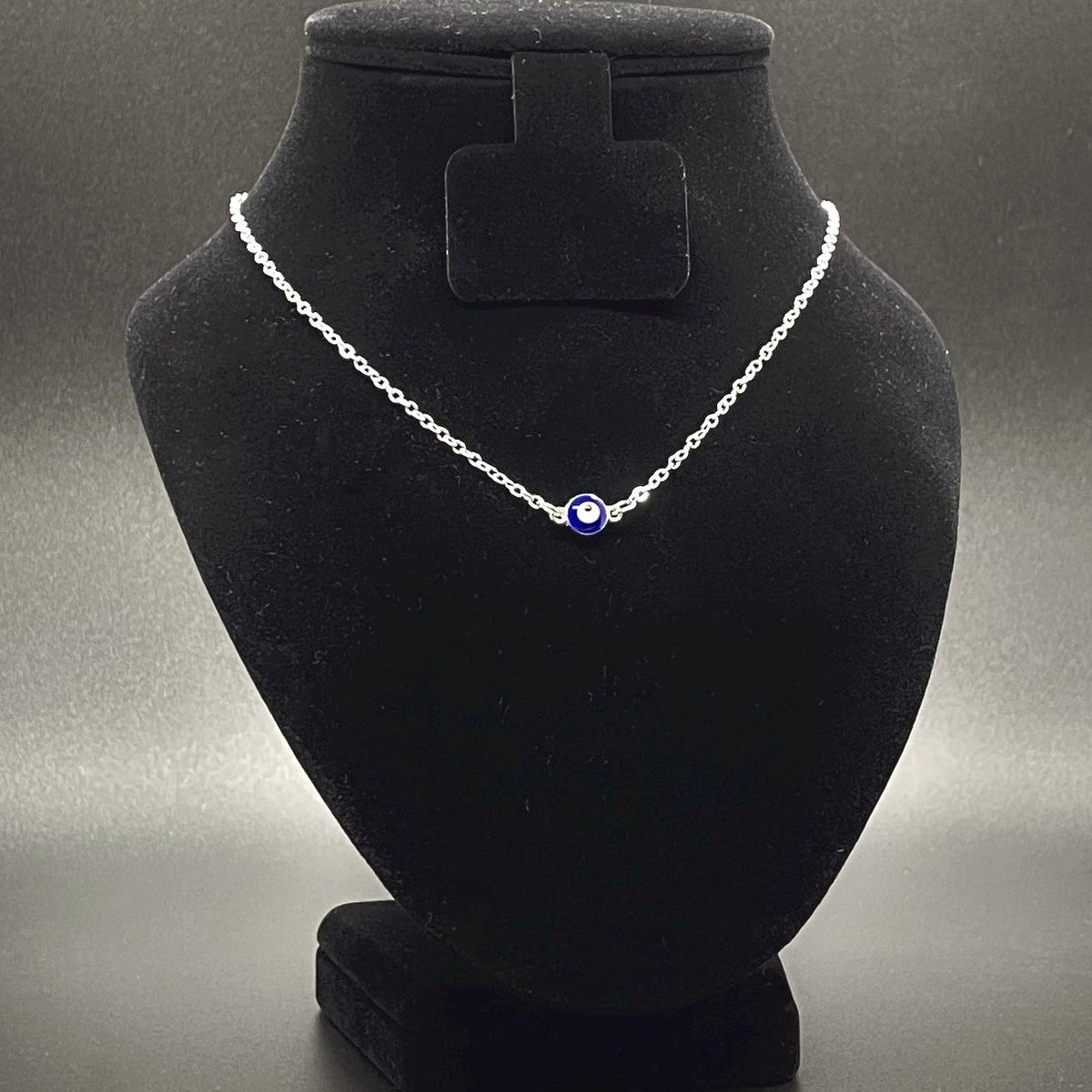 Evil Eye Necklace with a tiny round enamel eye charm on a black velvet bust against a gray background